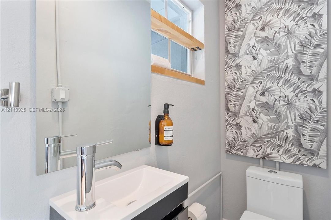 Wall-mounted vanity with rectangular sink, chrome single-handle faucet, large frameless mirror, integrated wood-finish shelving, and patterned wall covering