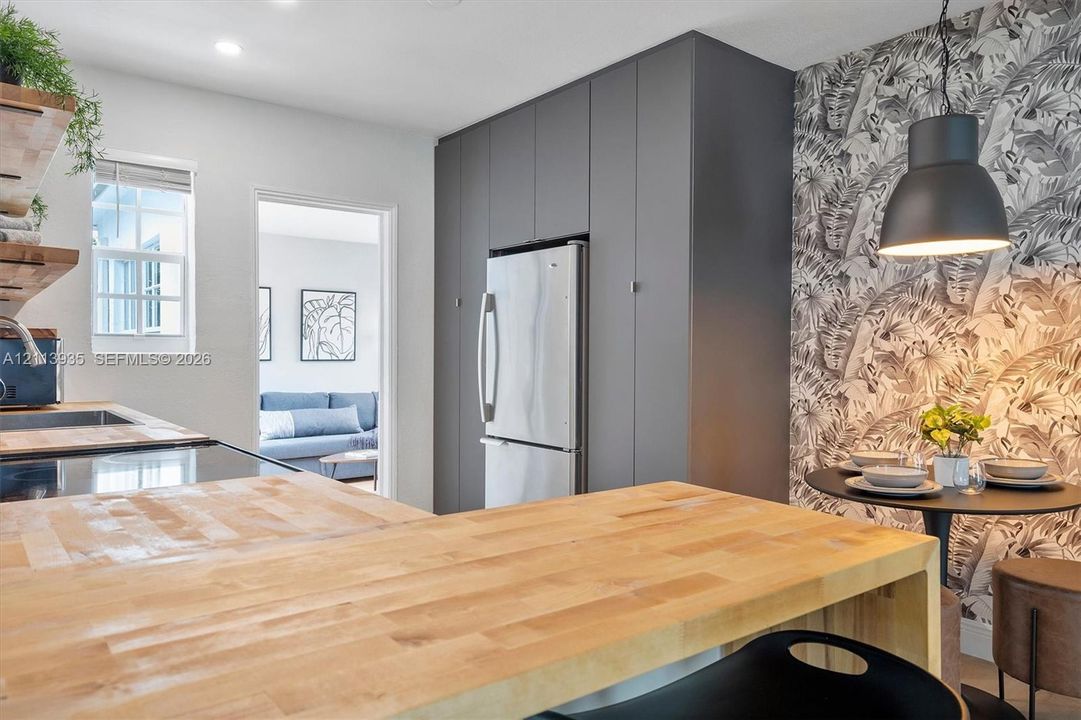 Kitchen featuring wood-finish butcher block countertops, floor-to-ceiling cabinetry, stainless steel refrigerator, patterned wall covering, and a matte black pendant light fixture