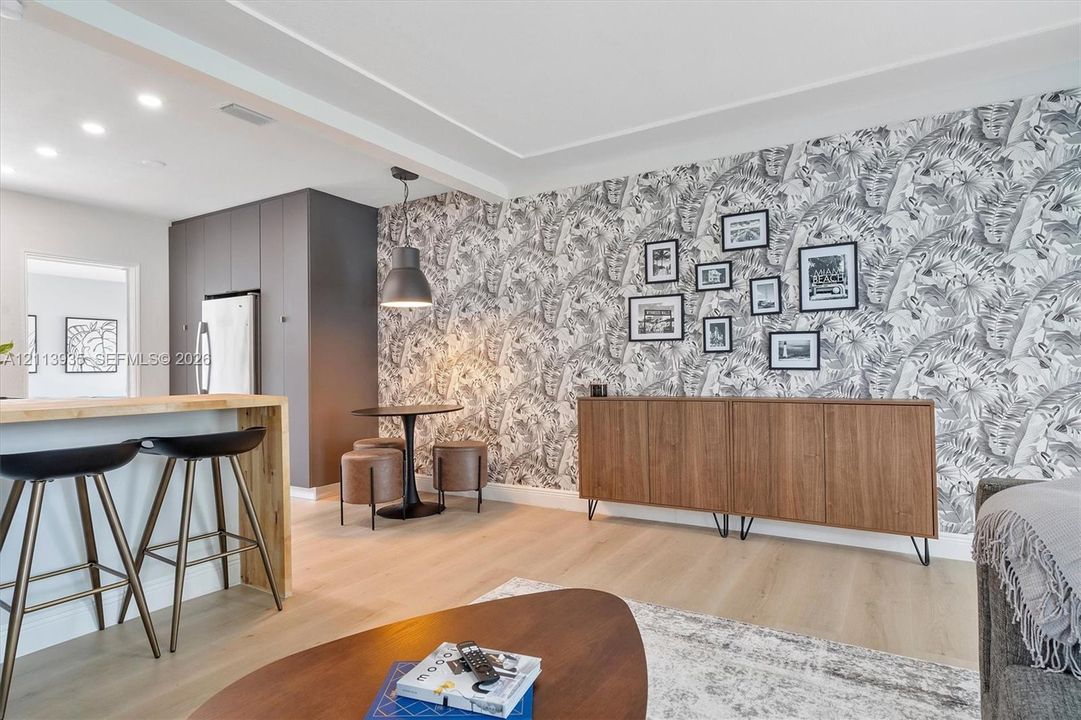 Open-concept space featuring light wood-finish flooring, recessed lighting, a modern pendant light, and a breakfast bar with a natural wood countertop
