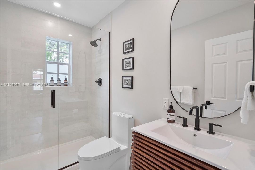 Bathroom featuring a slatted wood-finish vanity, oval mirror with a black frame, walk-in shower with a glass enclosure and black hardware, and matte black fixtures