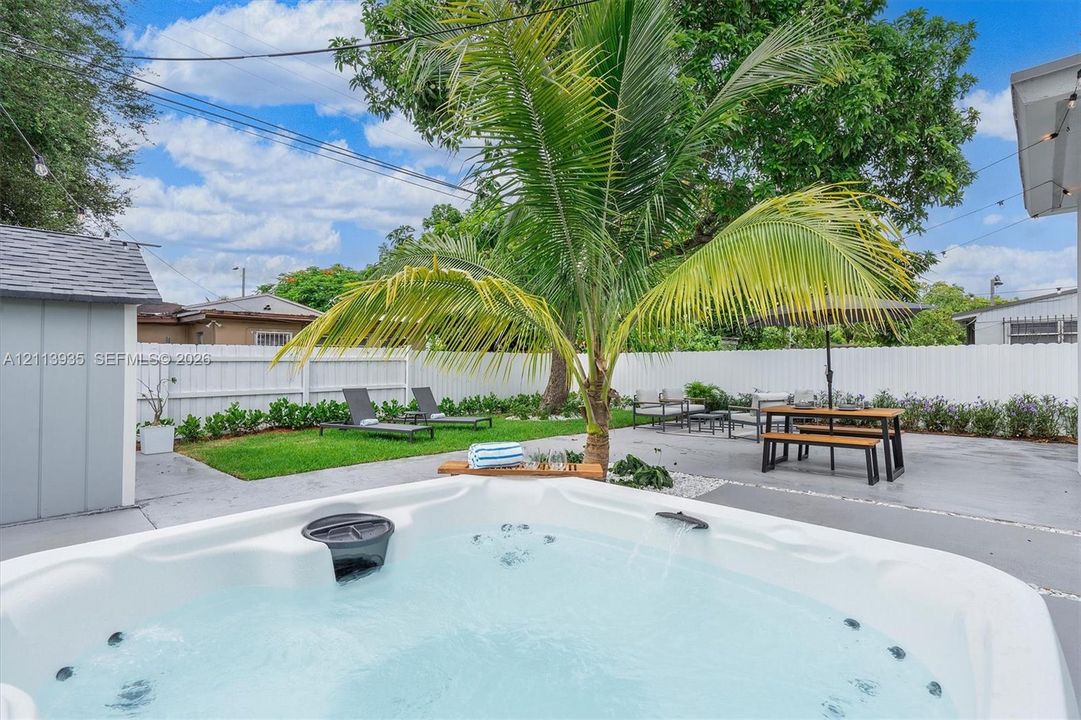 Enclosed backyard featuring an integrated hot tub, concrete patio, white vinyl fencing, and a mature palm tree