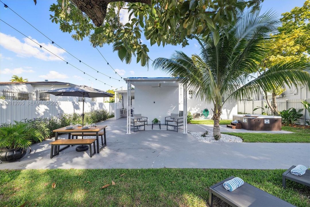 Fenced backyard featuring a concrete patio, covered lanai, built-in hot tub, and mature landscaping