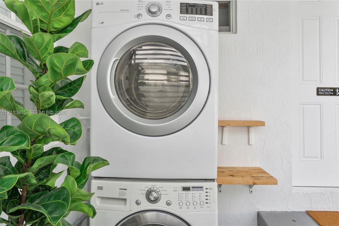 Stacked front-load washer and dryer unit with dual wood-finish wall-mounted shelving and white textured wall finish