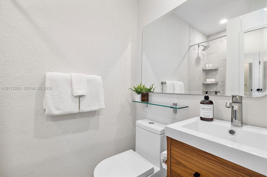 Bathroom featuring a wood-finish vanity with a rectangular sink, polished chrome faucet, large wall-mounted mirror, and glass shelving