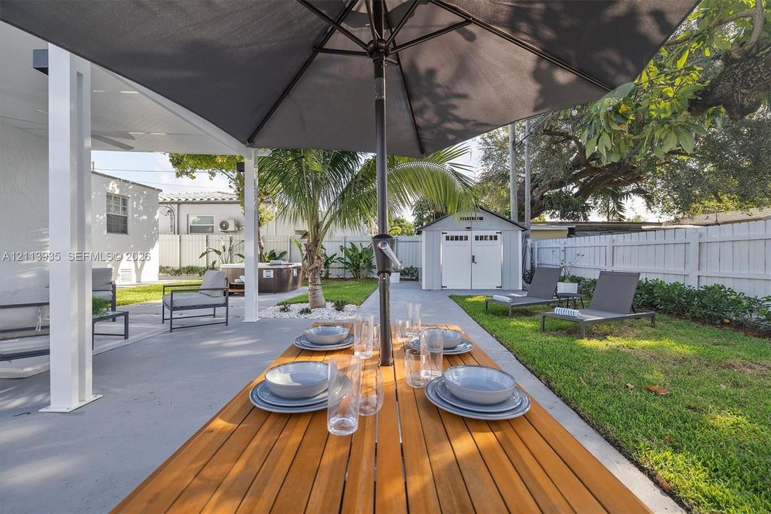 Covered patio featuring concrete flooring, manicured lawn, perimeter fencing, and a detached storage structure