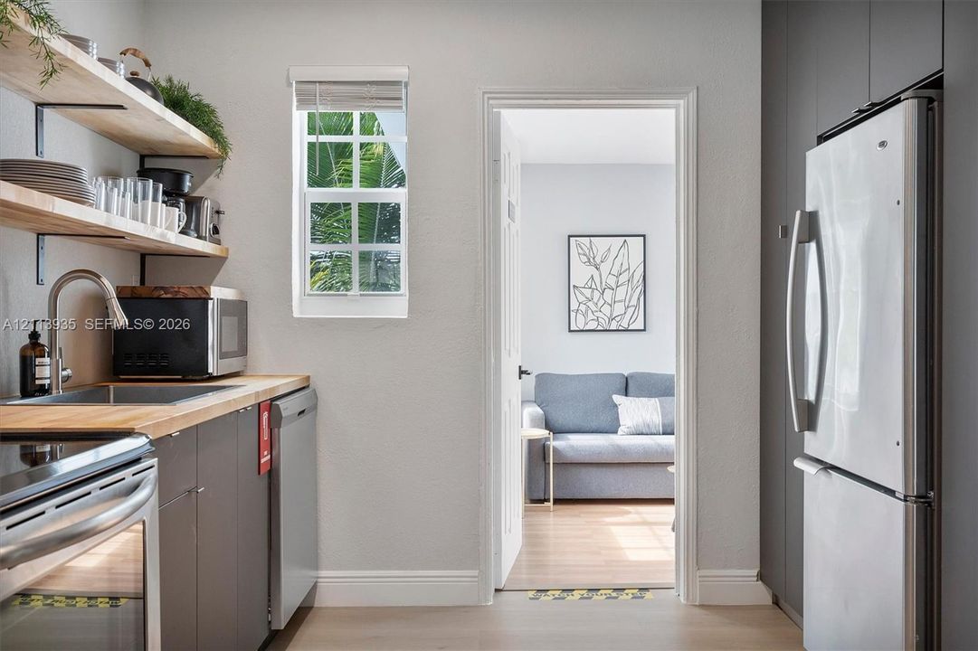 Kitchen featuring wood-finish countertops, open wood shelving, dark cabinetry, stainless steel appliances, and a window with muntin detailing