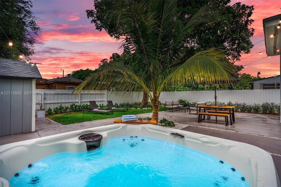 Backyard featuring a built-in hot tub, concrete patio, perimeter privacy fencing, manicured lawn, and mature palm tree