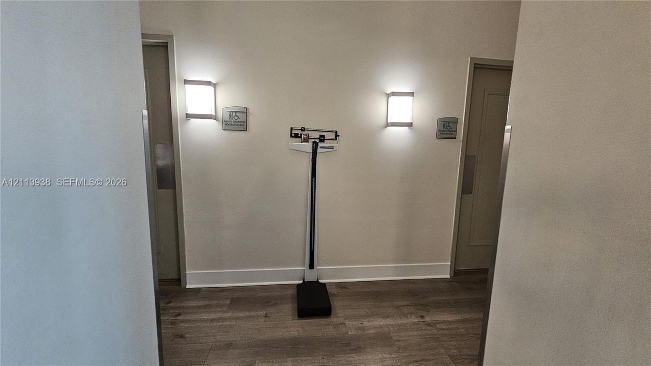 Interior hall featuring wood-finish flooring, two wall-mounted rectangular light fixtures, and dual entryways with brushed metal door plates