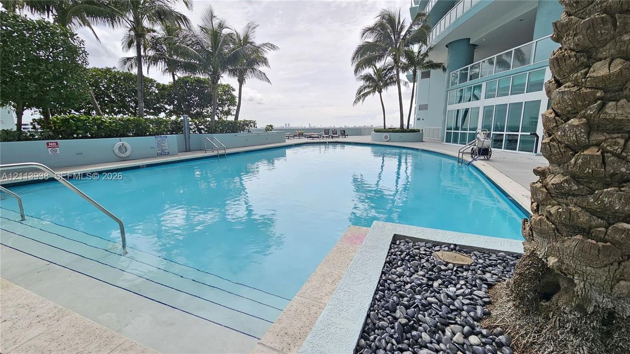 Swimming pool featuring tiered steps, metal handrails, and a stone-paver deck with a built-in stone landscaping border