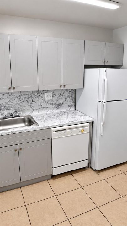Shaker-style cabinetry in a neutral finish, stone-patterned laminate countertop, stainless steel sink with dual-handle faucet, integrated dishwasher, and ceramic tile flooring