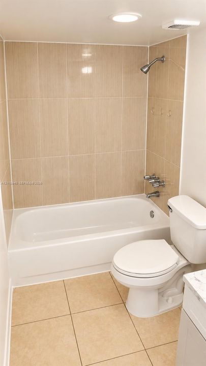 Bathtub with a shower head, tiled wall surround, square floor tiles, and a white toilet