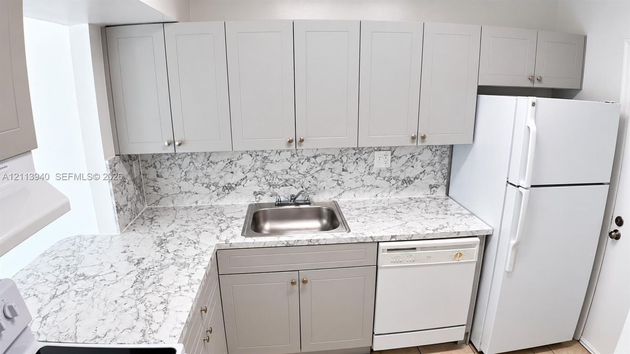 Kitchen featuring shaker-style cabinetry, patterned stone-look countertops, matching full-height backsplash, stainless steel drop-in sink, and a built-in dishwasher