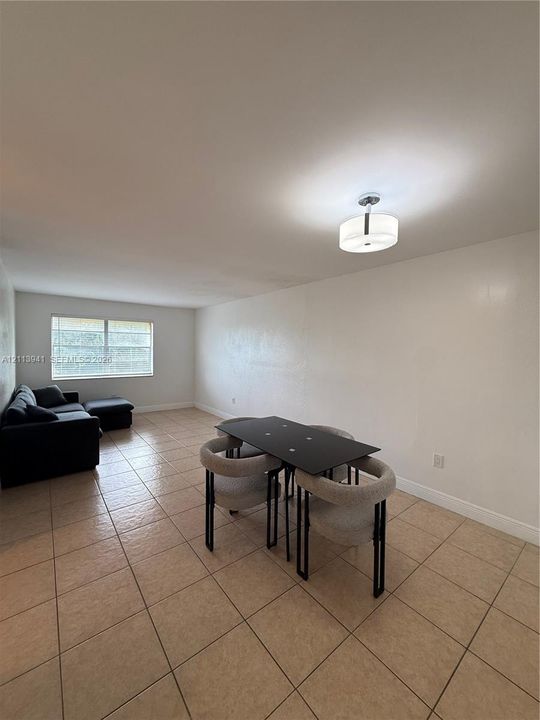 Open-concept room featuring neutral wall finishes, tile flooring, a large window, and a modern drum-style flush-mount ceiling light fixture