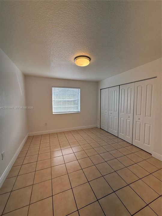 Neutral-toned tile flooring, multi-panel closet doors, and flush-mount ceiling lighting