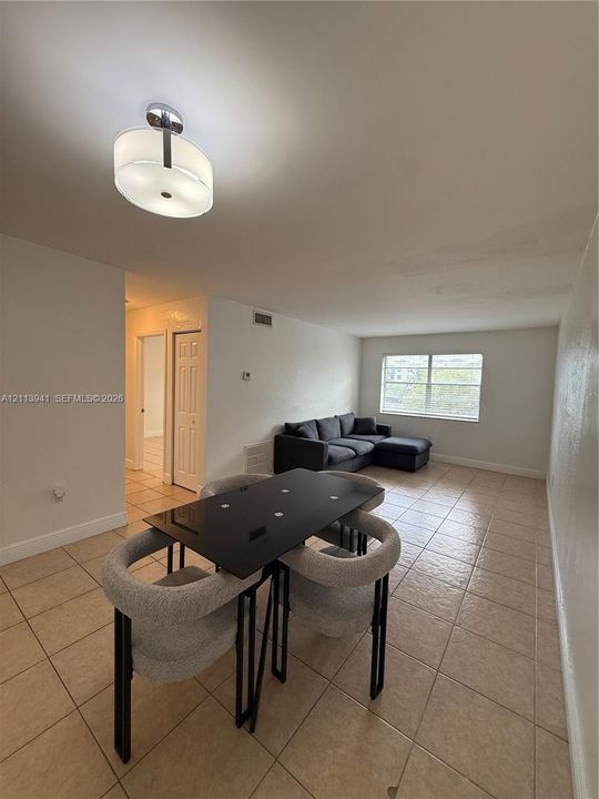 Open-concept room featuring light-toned tile flooring, a drum-style ceiling light fixture, and a large multi-pane window