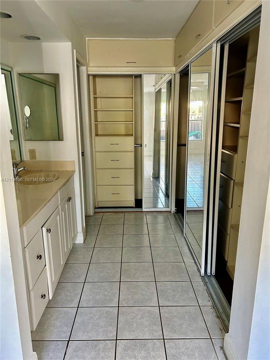 Vanity featuring a solid-surface countertop and integrated sink, complemented by built-in floor-to-ceiling cabinetry, sliding mirrored closet doors, and ceramic tile flooring