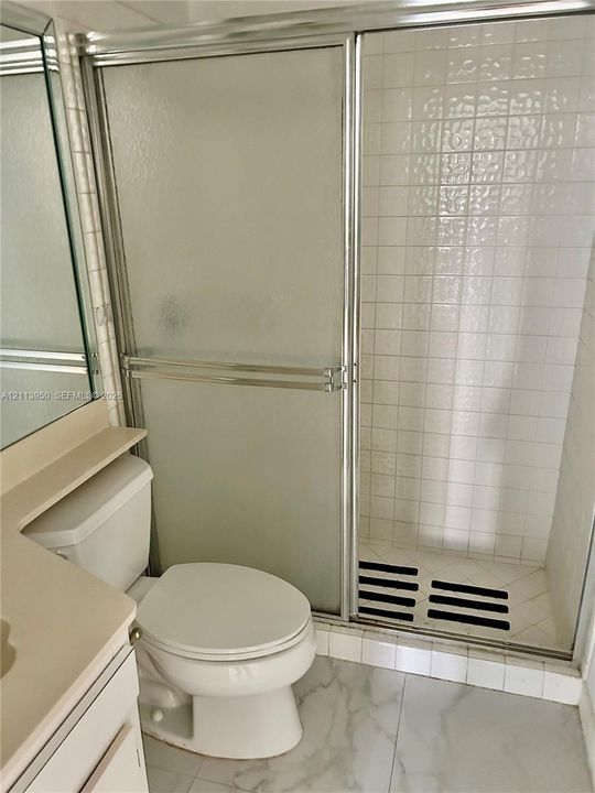 Bathroom featuring a shower stall with a sliding glass door and tiled surround, white vanity, and stone-finish flooring