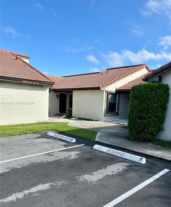 Stucco exterior with a tiled roof, featuring assigned parking spaces and a concrete walkway