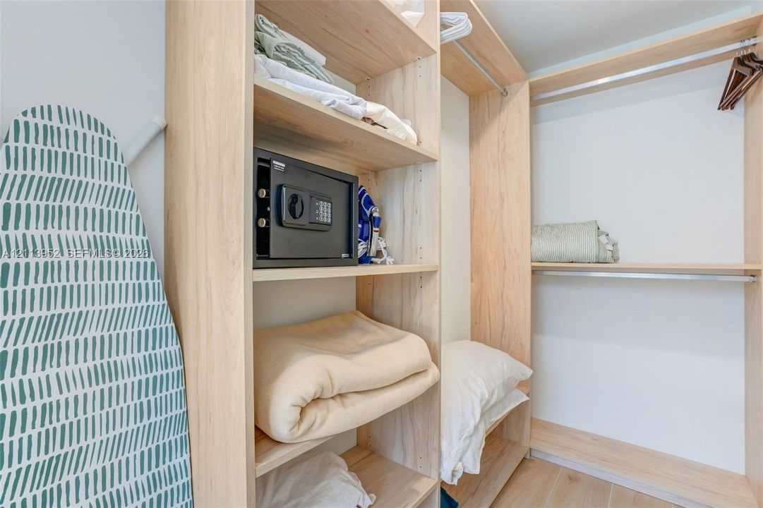 Customized reach-in closet featuring light-toned wood-finish shelving, multiple storage compartments, and integrated metal clothing rods