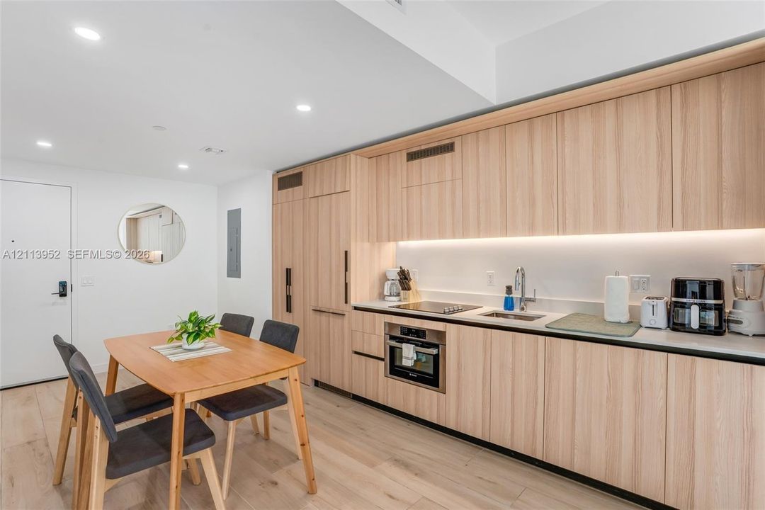 Modern kitchen featuring light wood-finish flat-panel cabinetry, integrated refrigerator, recessed lighting, and wood-finish flooring
