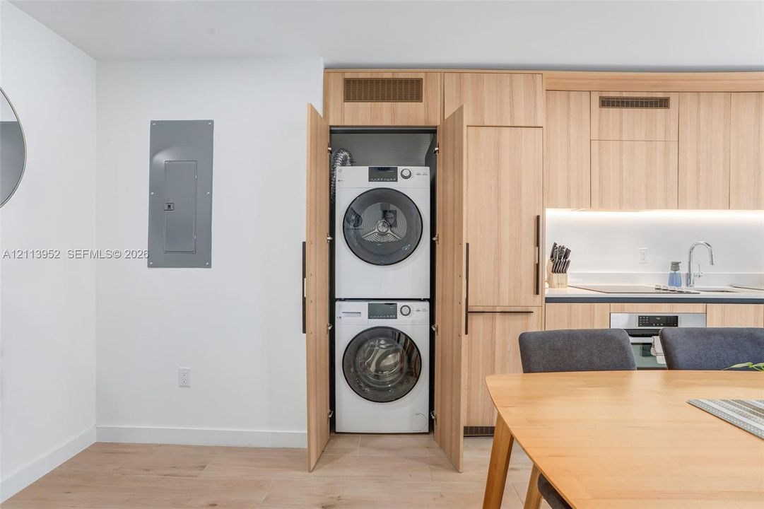 Built-in stacked laundry closet with wood-finish cabinetry, integrated cabinetry, light-toned wood-finish flooring, and recessed under-cabinet lighting