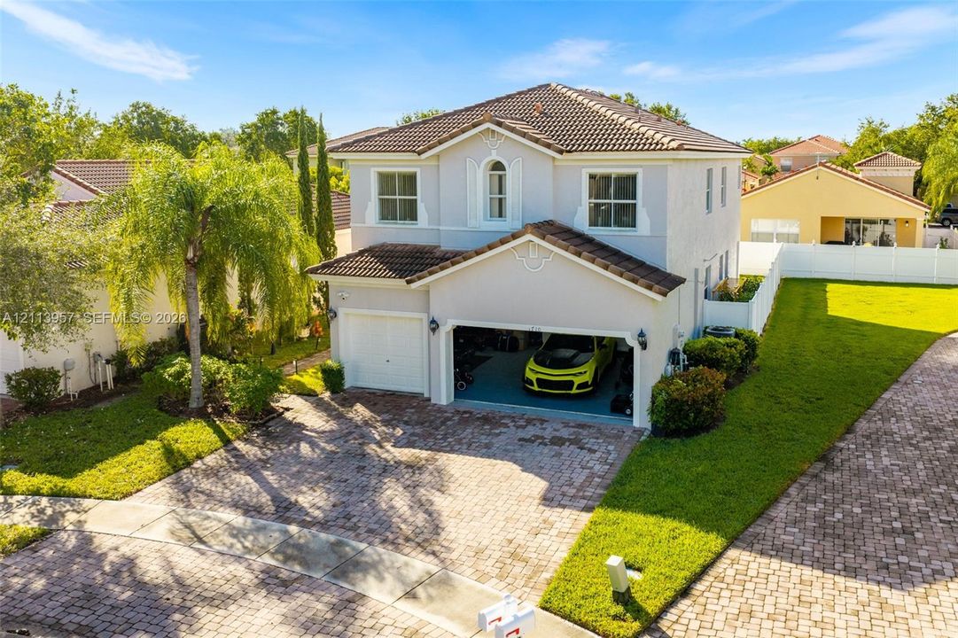 Two-story residence featuring a tile roof, light-toned exterior finish, paver driveway, and a two-car garage