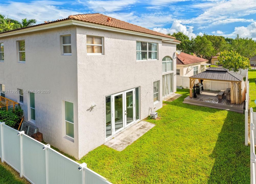 Two-story stucco exterior with a tile roof, French glass doors, concrete patio, and a fenced backyard featuring a detached gazebo on a wood-composite deck