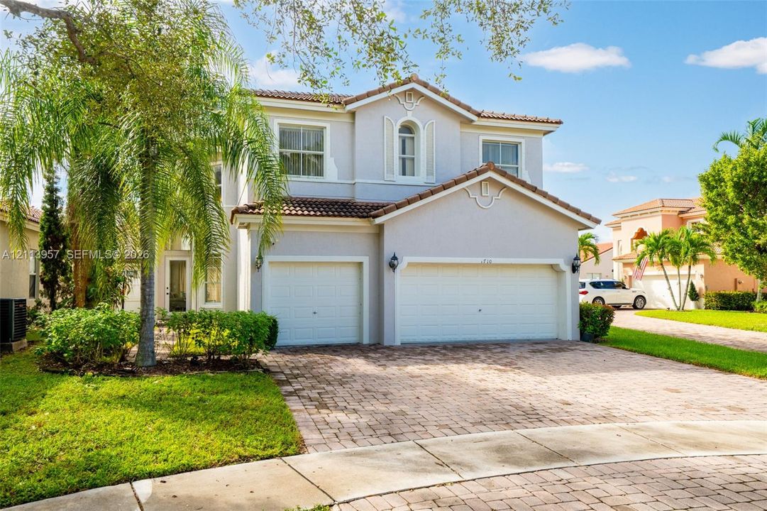 Two-story exterior featuring a clay tile roof, stucco finish, arched window detailing, and a two-car garage with a paved driveway