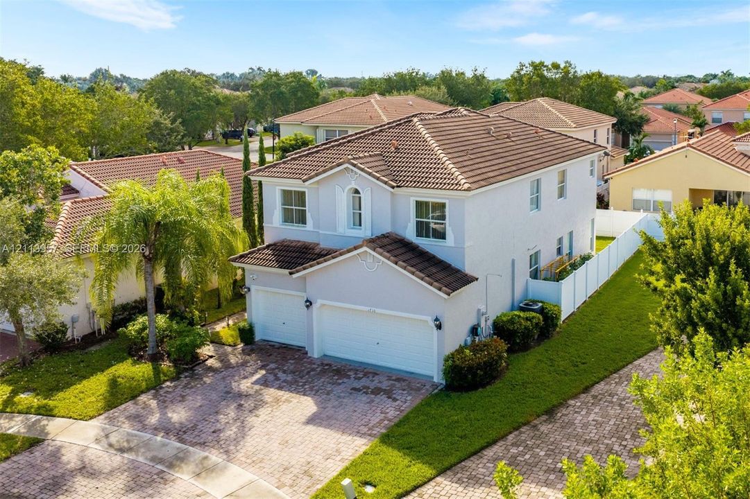Two-story stucco exterior featuring a multi-gabled tile roof, an attached two-car garage, and a paved stone driveway
