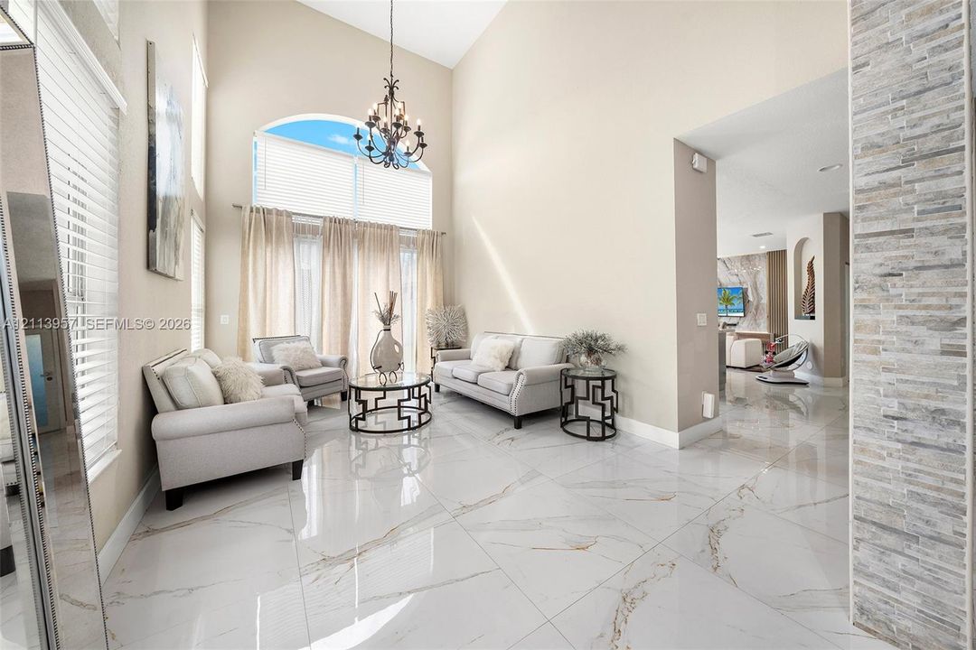 High-ceiling living area featuring large-format polished porcelain tile flooring, architectural stacked-stone accent wall, arched wall niche, and a multi-light metal chandelier