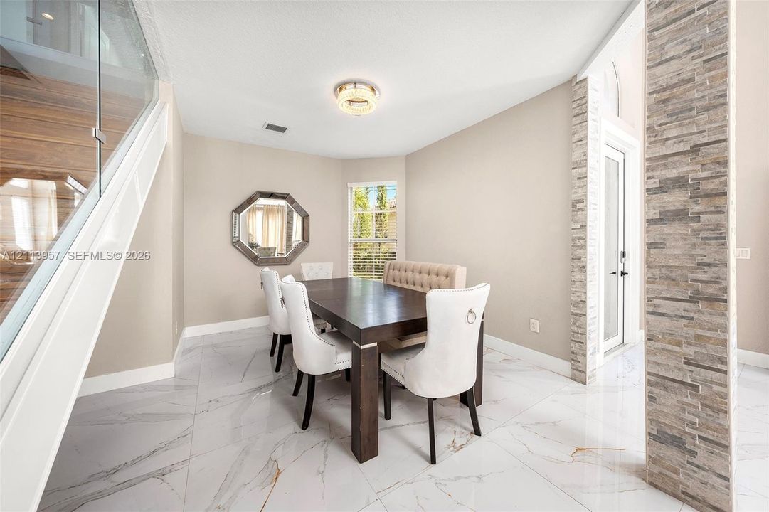 Polished tile flooring with veining, floor-to-ceiling textured stone accent pillar, glass panel staircase railing, and flush-mount LED circular light fixture