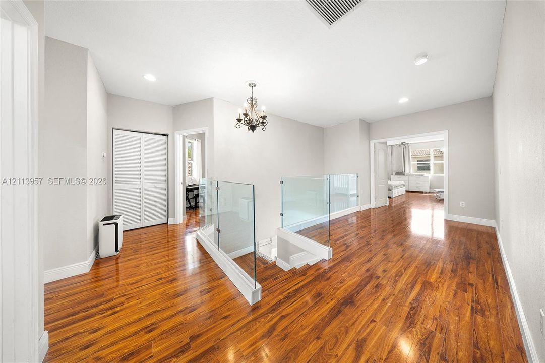 Interior space featuring wood-finish flooring, glass panel stair railing, recessed lighting, and a multi-light chandelier