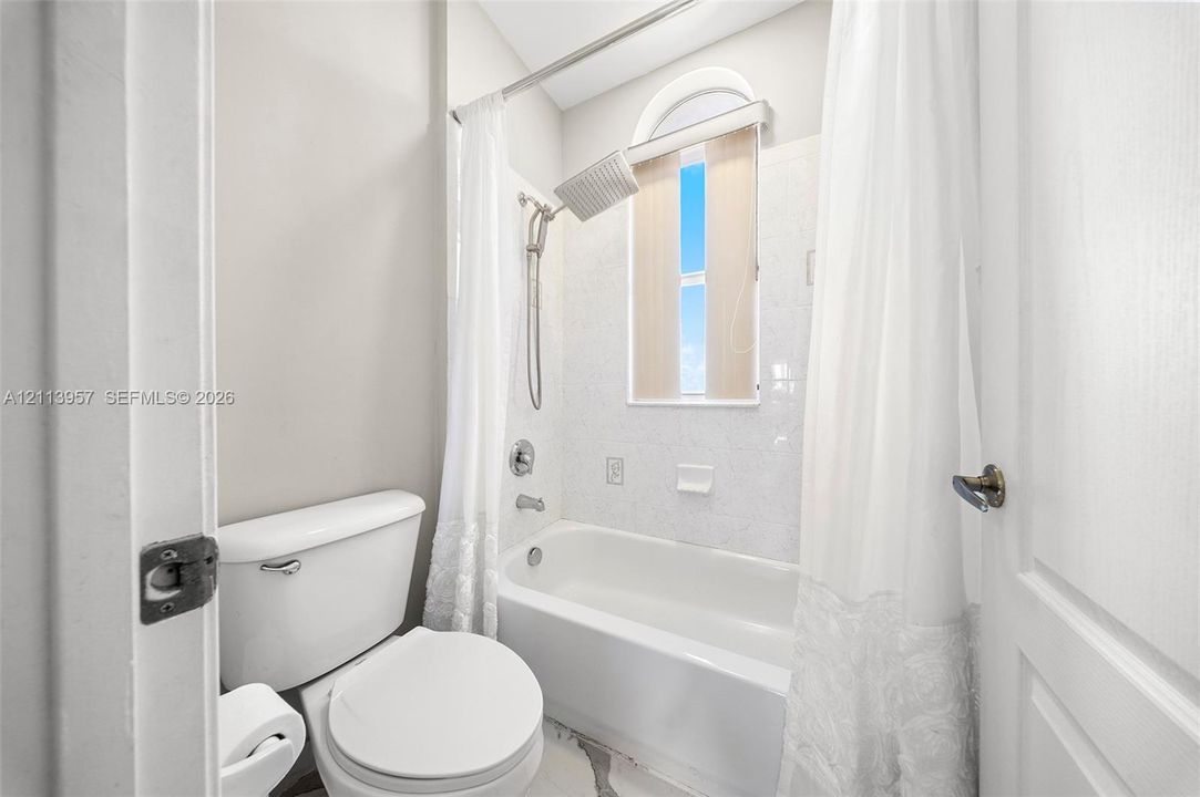 Bathroom featuring a porcelain bathtub with a shower head, arched window with a transom, and light-toned tile wall surround