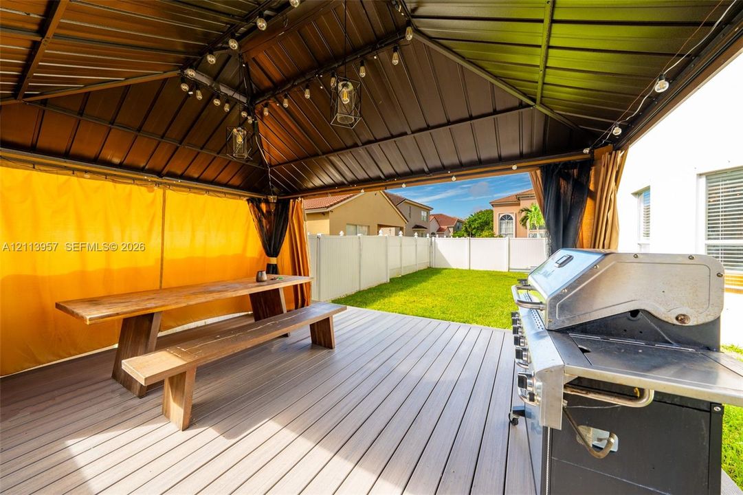Outdoor living area featuring a covered gazebo with a metal roof, composite decking, and a built-in outdoor grill