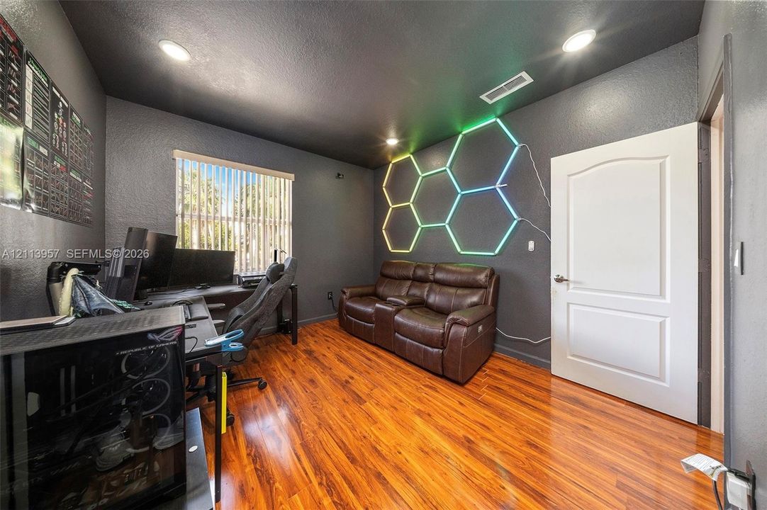Interior room featuring wood-finish flooring, dark-toned walls, recessed lighting, and a window with vertical blinds