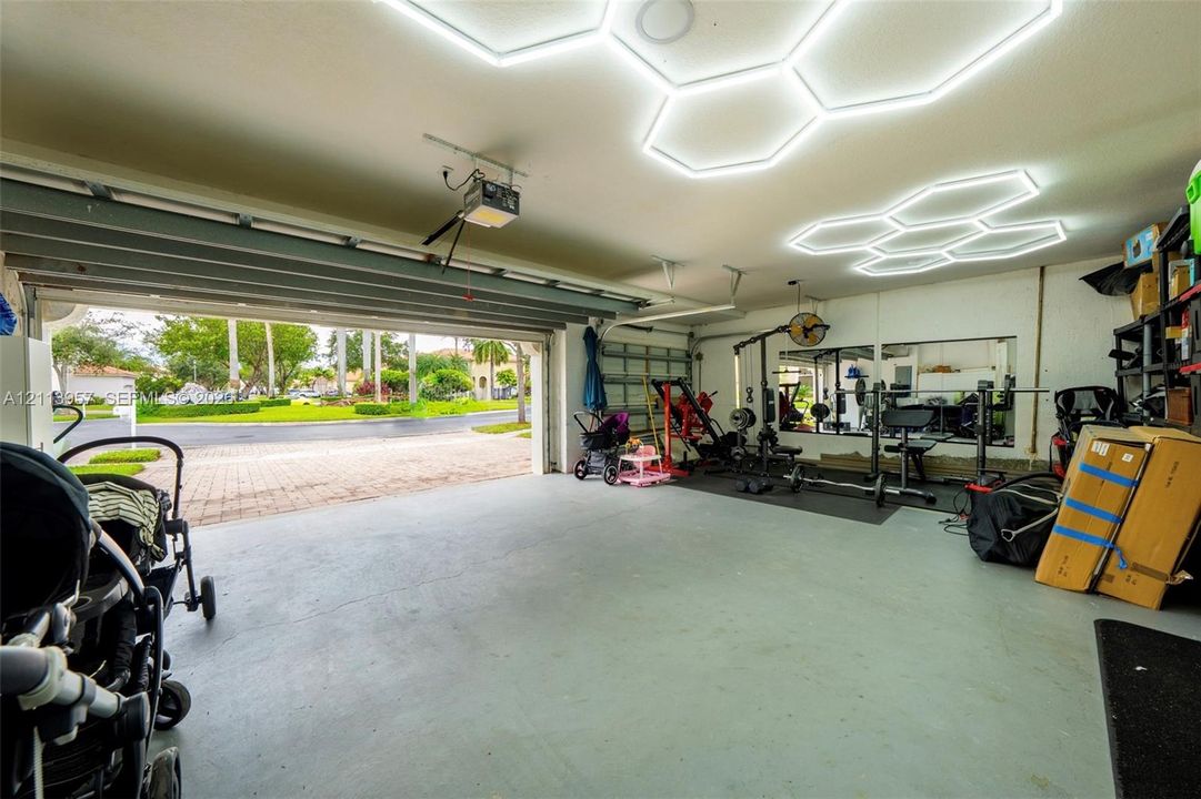 Multi-vehicle garage featuring hexagon-patterned LED overhead lighting, painted concrete flooring, and a wide-span door