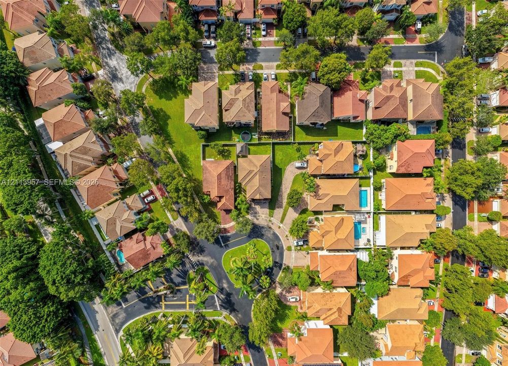 Aerial perspective of a residential neighborhood featuring cul-de-sac streets, densely wooded areas, paved driveways, and homes with pitched tile roofing