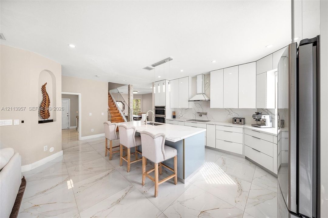 Kitchen featuring high-gloss white cabinetry, quartz countertops, a central island with integrated sink, recessed lighting, and large-format porcelain tile flooring