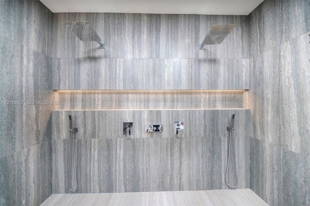 Walk-in shower featuring floor-to-ceiling stone tile, dual rainfall showerheads, integrated recessed lighting, and two wall-mounted hand-held sprayers
