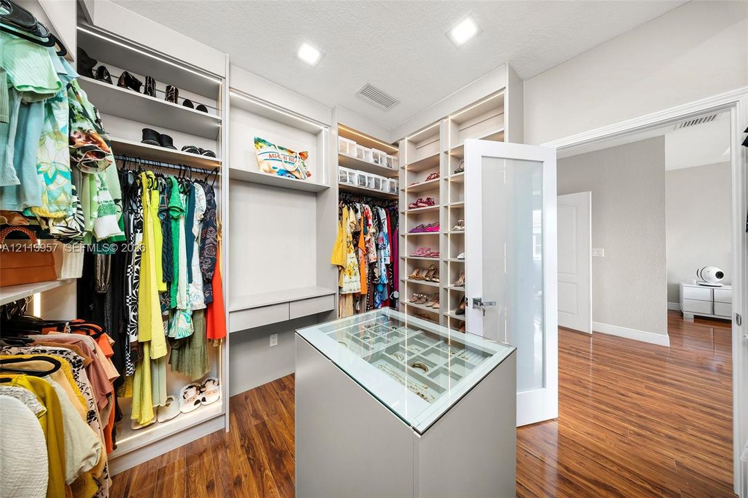 Walk-in closet featuring extensive built-in shelving, a central storage island with a glass display top, recessed lighting, and wood-finish flooring