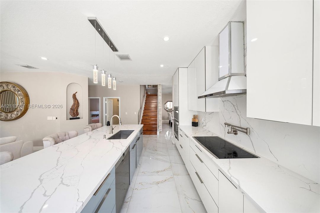 Kitchen featuring quartz countertops, flat-panel cabinetry, a stainless steel chimney hood, a pot filler faucet, and large-format porcelain tile flooring
