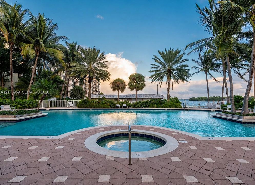 Inground swimming pool with tiled coping, integrated spa, and geometric paver decking surrounded by mature palm trees
