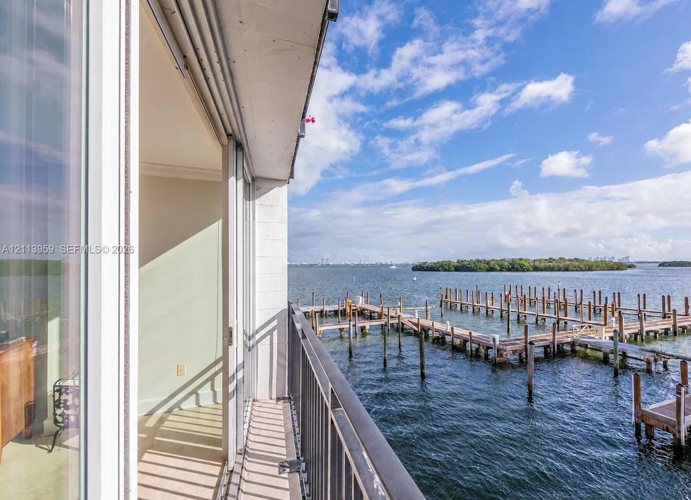 Private balcony featuring a metal railing and sliding glass door access, overlooking the water and wooden pier structures