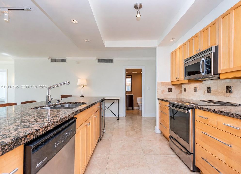 Kitchen featuring natural wood cabinetry, stone countertops, stainless steel appliances, a double-basin undermount sink, and stone tile flooring