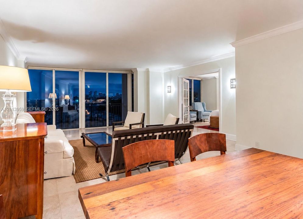 Expansive interior space featuring crown molding, polished stone flooring, recessed lighting, wall-mounted sconces, and floor-to-ceiling glass sliding doors