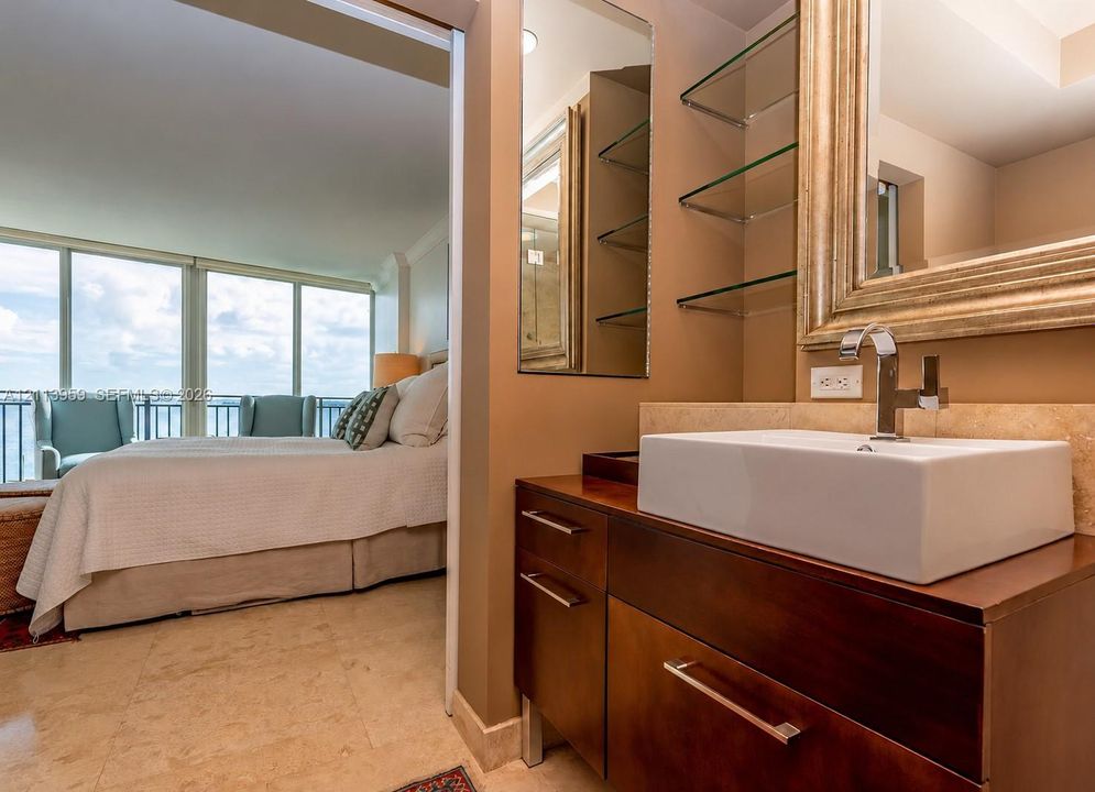 Modern vanity featuring a rectangular vessel sink, polished chrome faucet, stone-surfaced backsplash, built-in glass shelving, and stone flooring