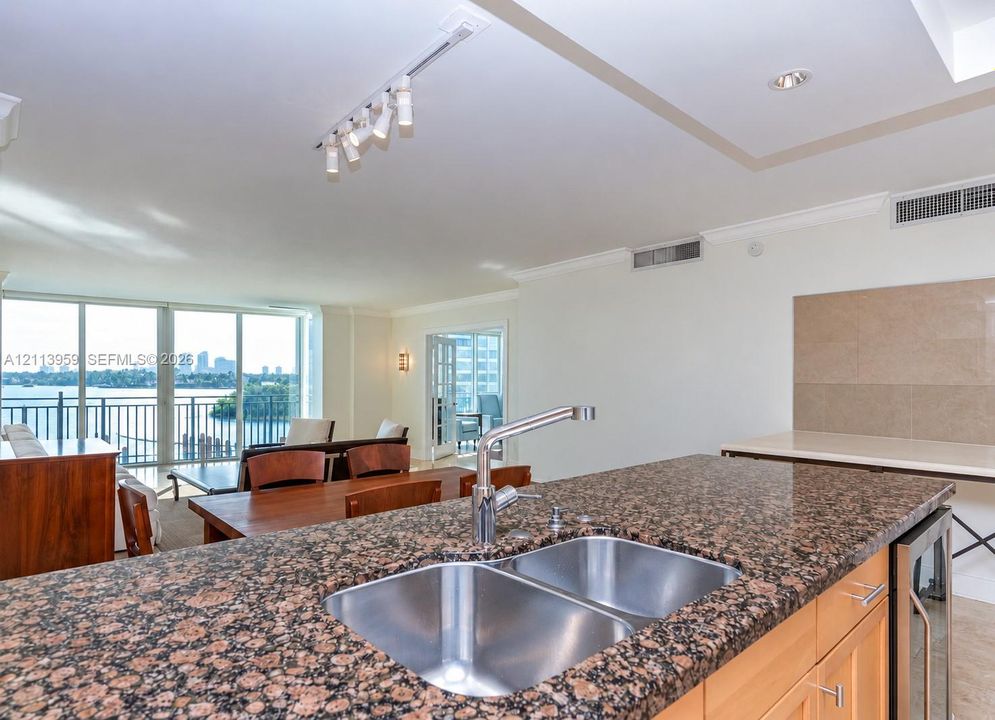 Kitchen island featuring speckled stone countertops, dual-basin stainless steel sink with a high-arc faucet, wood-finish cabinetry, and built-in beverage refrigerator
