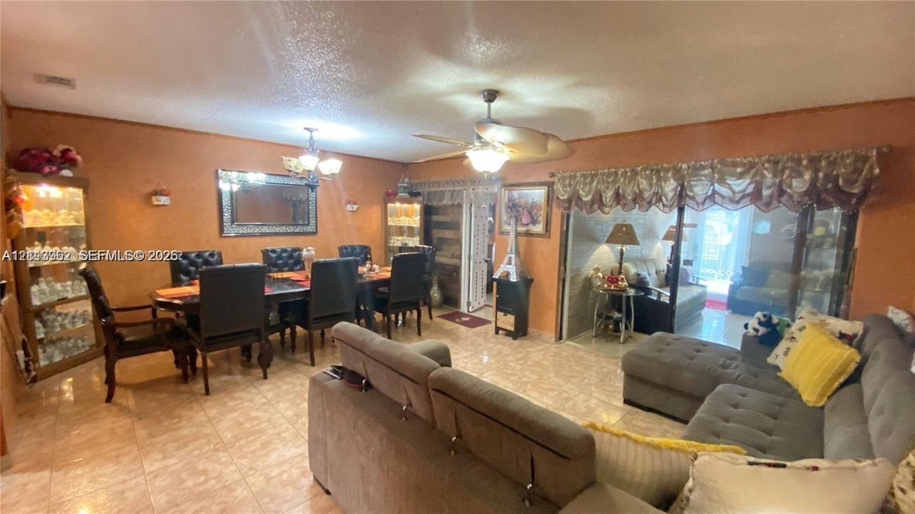 Open-concept interior featuring light-toned tile flooring, recessed lighting, dual ceiling fans, and sliding glass doors with overhead valance trim