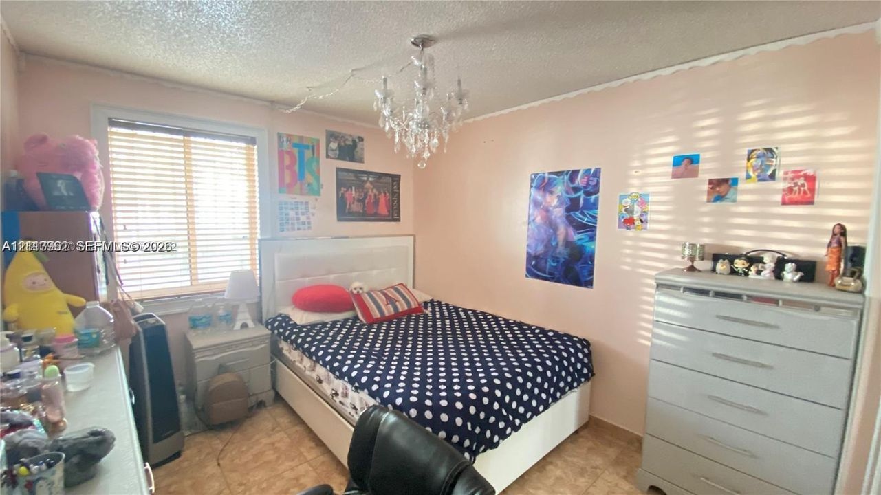 Room featuring horizontal blinds, tile flooring, and a central crystal-style chandelier fixture