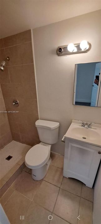 Bathroom featuring a tiled shower enclosure, white vanity cabinet with a integrated sink, two-light wall-mounted fixture, and ceramic floor tiling
